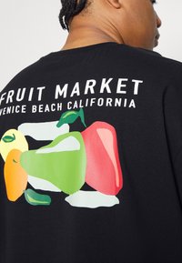 T-shirt nera a maniche corte con grafiche di frutta colorata in giallo, verde, rosso e rosa, con la scritta "FRUIT MARKET" sopra in bianco.