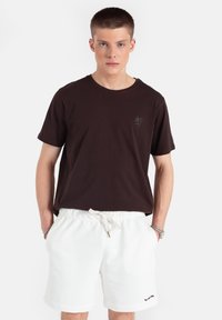 Ciemnobrązowa bawełniana koszulka z małym logo palmy na piersi, w połączeniu z białymi szortami z polaru z troczkiem i bocznymi kieszeniami.