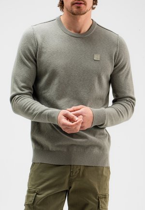 Grijze gebreide trui met een ronde hals, ribbed manchet en zoom, met een klein stoffen logo patch op de borst. Gemaakt boven een olijfgroene cargobroek.