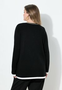 Suéter negro de punto con cuello redondo, que presenta ribetes blancos en los puños y el dobladillo, y un acabado texturizado en la tela.