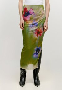 Maxi-Rock mit floralen Drucken in Grün, der pinke, blaue und rote Farbtöne aufweist und ein dekoratives Design hat. Kombiniert mit schwarzen knielangen Stiefeln.
