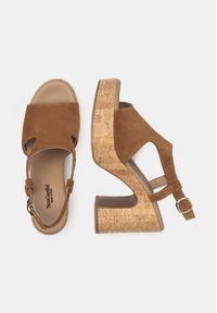 Sandales à talons en daim marron avec une plateforme en liège. Elles présentent un bout ouvert, une bride de cheville avec une boucle, et un design supérieur texturé.