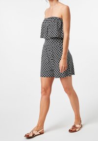 Robe sans manches à motifs noir et blanc avec un haut en volants superposés, une taille cintrée, une jupe évasée et une silhouette décontractée, accompagnée de sandales plates.