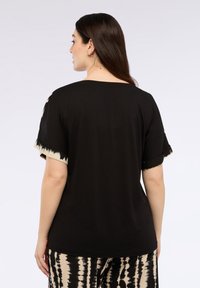 Camiseta negra de manga corta con un patrón de teñido anudado en beige y negro en los dobladillos de las mangas. Material de algodón suave, corte relajado.