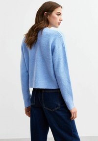 Maglione corto blu chiaro realizzato in tessuto morbido e con texture, dotato di maniche lunghe, abbinato a jeans scuri a vita alta.
