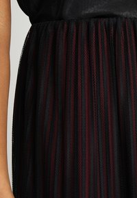 Gonna in tulle nera con strisce verticali testurizzate di bordeaux. Il tessuto ha un aspetto trasparente e stratificato per un effetto voluminoso.