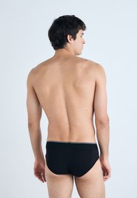 Zwarte katoenen slip met een aansluitend ontwerp, voorzien van een witte elastische tailleband, een gladde textuur en een lage snit aan de achterkant.