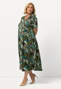 Maxikleid mit floralem, grün-braunem Muster, kurzen Ärmeln, V-Ausschnitt und weichem Stoff. Kombiniert mit hellbeigen High Heels.
