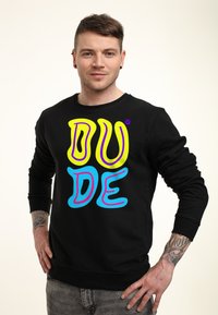 Sudadera negra con el texto "DUDE" en colores llamativos: amarillo, rosa y azul. Cuenta con cuello redondo y puños ajustados, fabricada en un tejido suave.