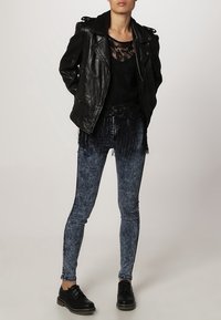 Svart läderbikerjacka, marinblå spetsblus, fransade blå skinny jeans och svarta snörskor. Funktioner inkluderar texturerade tyger och fransar.