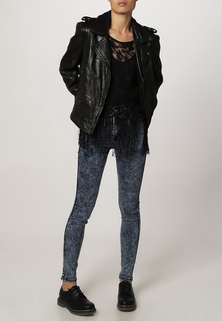 Svart läderbikerjacka, marinblå spetsblus, fransade blå skinny jeans och svarta snörskor. Funktioner inkluderar texturerade tyger och fransar.