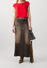 Rode top met korte mouwen gecombineerd met een lange bruin ombre spijkerrok. Accessoires omvatten een zwarte bewerkte handtas en bruine kniehoge laarzen.