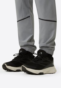 Pantofi sport negri cu partea superioară din plasă și talpă albă, asortați cu pantaloni jogger gri cu manșete elastice și accente negre.