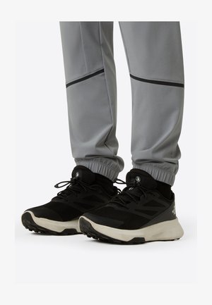 Schwarze Sportsneaker mit Mesh-Obermaterial und weißer Sohle, kombiniert mit grauen Jogginghosen mit elastischen Bündchen und schwarzen Akzenten.