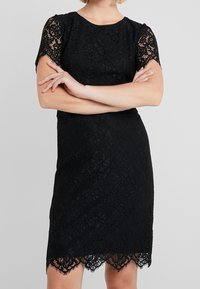 Schwarzes Spitzenkleid mit kurzen Ärmeln, floralem Muster, gewelltem Saum, taillierter Silhouette und strukturiertem Oberflächenmaterial.