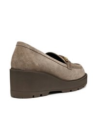 Zapatos de cuña en ante marrón claro con punta redondeada, correa decorativa y suela de goma texturizada. Presentan un ligero tacón para mayor elevación.