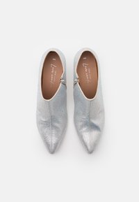 Un paio di scarpe slip-on argentate con punta appuntita, decorate con scintillanti strass e cerniere laterali su uno sfondo bianco.
