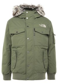 Veste d'hiver isolante vert olive avec capuche bordée de fourrure, multiples poches à rabat, poignets côtelés, et logo The North Face sur la poitrine.