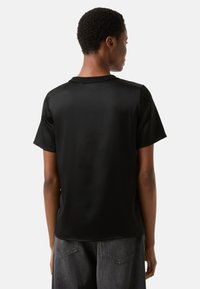 Schwarzes Kurzarmshirt mit glatter Textur, Rundhalsausschnitt und lockerem Schnitt. Rückansicht zeigt ein schlichtes Design und weichen Stoff.