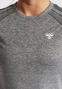 Szara sportowa koszulka z teksturowanej tkaniny, z poziomymi paskami i małym białym logo na piersi. Okrągły dekolt i krótkie rękawy.