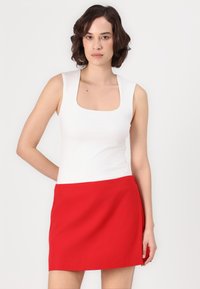Top alb fără mâneci cu decolteu pătrat, asortat cu o fustă mini roșie. Material neted, design ajustat, linii curate și fără modele vizibile.