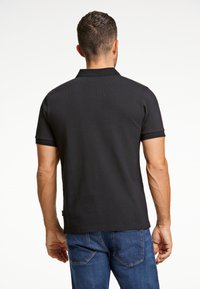 Svart polo-tröja med en strukturerad väv, korta ärmar och klassisk krage. Kombinerad med blå jeans med synliga sömdetaljer.