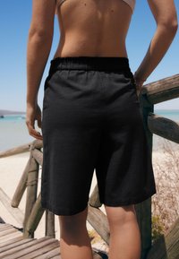 Sorte knælange shorts lavet af letvægtsstof; har elastisk talje og glat tekstur, velegnet til varmt vejr.