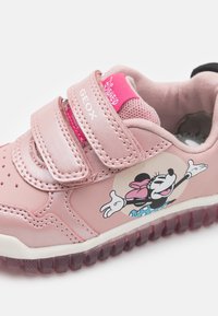 Rosa Kinderturnschuhe mit zwei Klettverschlüssen, versehen mit einem Minnie-Maus-Motiv. Glattes Leder-Obermaterial, strukturierte Gummisohle und Mesh-Einsätze.