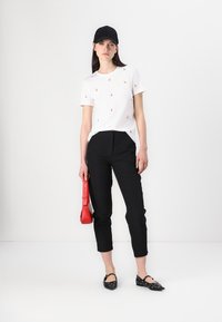 Witte t-shirt met korte mouwen en kleine bloemenpatronen, zwarte op maat gemaakte broek, rode handtas en zwarte platte schoenen met decoratieve accenten.