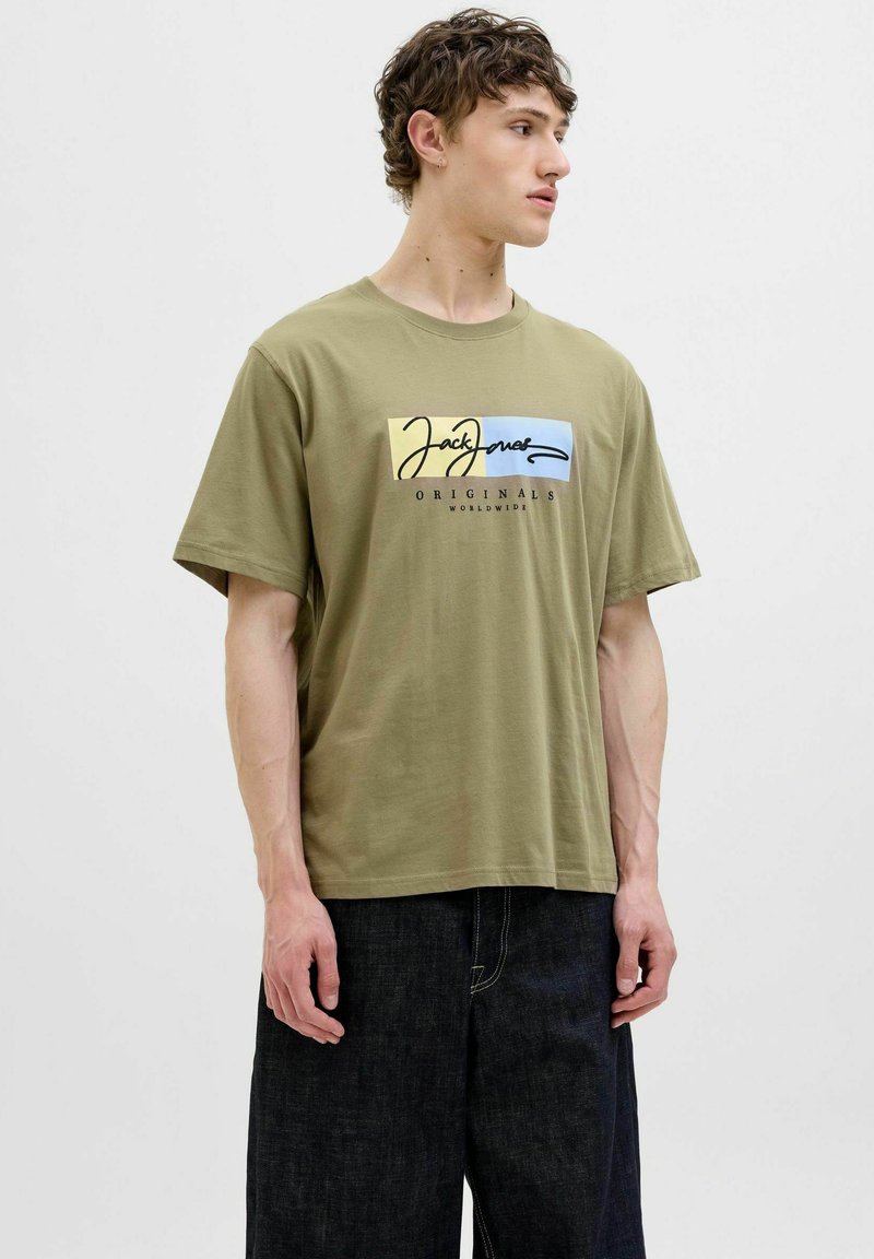 Olivengrøn bomulds t-shirt med korte ærmer, der har et flerfarvet logodesign på forsiden, parret med mørk denim bukser.