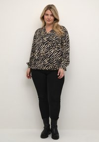 Blusa animalier nera e beige con scollatura a V, maniche lunghe e vestibilità morbida. Abbinata a pantaloni neri aderenti e stivali neri chunky.