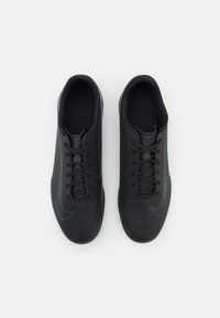 Baskets de sport noires avec un dessus texturé, présentant un bout lisse, des lacets foncés et des accents bleus discrets sur les côtés.