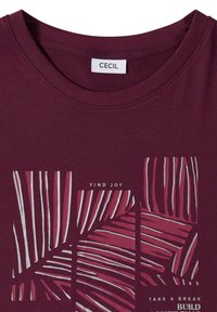 T-shirt marron avec étiquette "CECIL", motif abstrait de feuilles roses et argentées, et texte indiquant "FIND JOY" et "TAKE A BREAK BUILD".