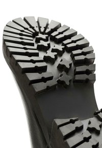 Suela de bota de goma negra con profundas ranuras, con patrones angulares y en forma de estrella, diseñados para ofrecer tracción y durabilidad.