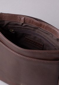 Brown faux leather bag interior with a zippered pocket. Interior lining is solid brown. Features a smooth texture and minimal stitching.