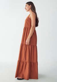 Vestido largo sin mangas de color marrón, hecho de una tela suave, con un diseño en capas que consta de tres secciones y un corte relajado.