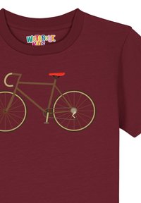 T-shirt bordeaux présentant un graphique d'un vélo marron avec une selle rouge, mettant en avant des roues circulaires et des éléments de design géométriques simples.