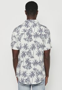 Camicia a maniche corte in tessuto bianco con motivo a foglie di palma blu navy, colletto button-down e orlo dritto, con una vestibilità comoda.