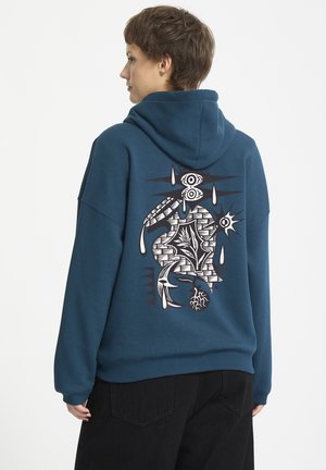 Teal hoodie met een groot zwart-wit grafisch ontwerp op de achterkant, met abstracte vormen, ogen en tranenmotieven. Zacht materiaal, relaxte pasvorm.