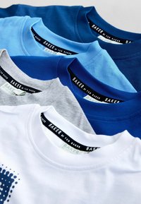 Quatre t-shirts superposés, avec les couleurs bleu marine, bleu clair, gris et blanc. Chacun possède un col rond et une étiquette intérieure de marque.