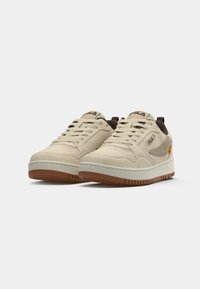 Beige semskinn sneakers med en hvit mellomsåle og gummisåle. Har en brun detalj og 'FILA' logo på tungen og siden.