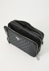 Pochette à carreaux noirs avec zips argentés et logo de la marque. Extérieur texturé, double compartiment et doublure en tissu lisse.