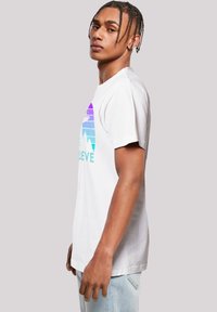 White cotton t-shirt with short sleeves, featuring a multi-colored mountain graphic and text "BELIEVE" in turquoise. Relaxed fit.