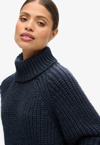 Granatowy sweter z dzianiny z wysokim, prążkowanym kołnierzem, teksturowanym wzorem i luźnym krojem, prezentujący grubą, przytulną tkaninę.