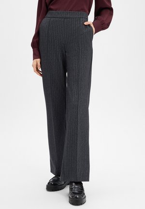 Pantalon à jambes larges en tissu gris foncé à rayures fines. Doté d'une taille haute et de poches latérales. Associé à des chaussures noires.