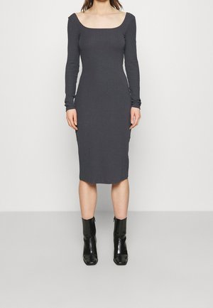 Dunkelgraues, geripptes Strickkleid mit quadratischem Ausschnitt, langen Ärmeln und taillierter Silhouette, das bis zur Mitte der Waden reicht. Kombiniert mit schwarzen Knöchelstiefeln.
