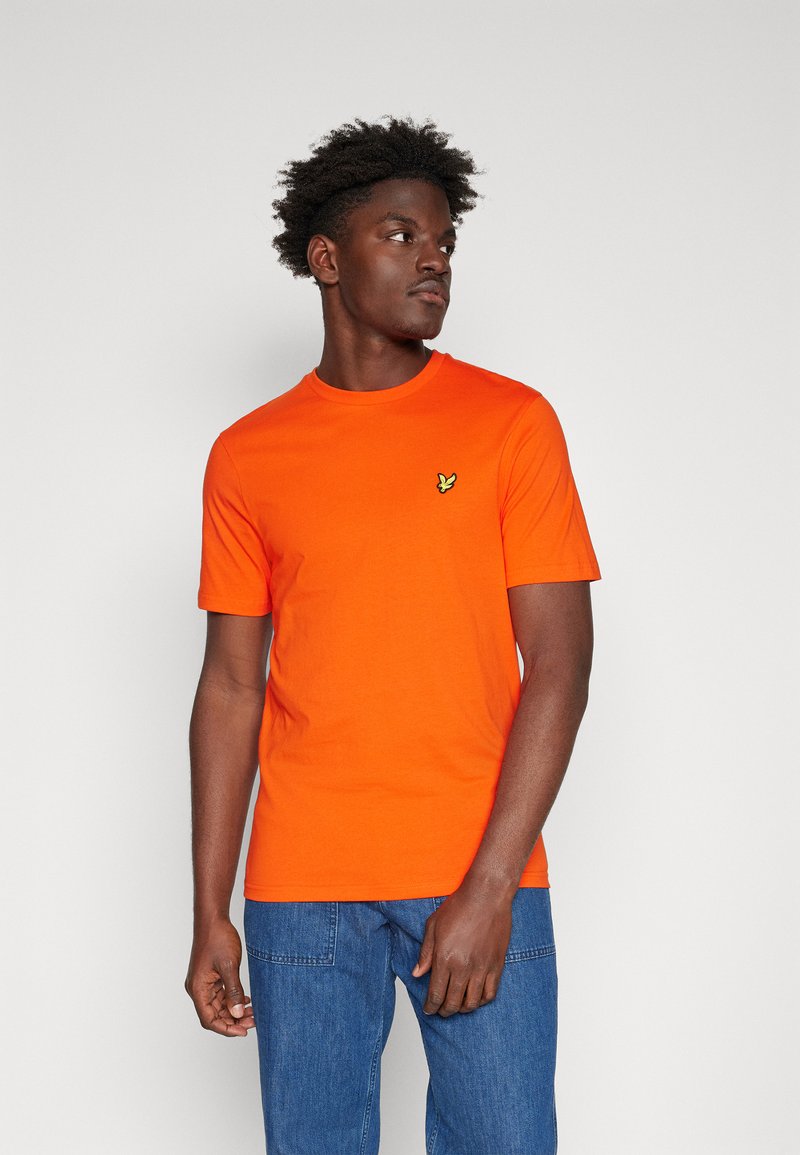 Helles oranges Baumwoll-T-Shirt mit Rundhalsausschnitt, kurzen Ärmeln und einem kleinen gelben Logo auf der linken Brust. Lässiger Schnitt.