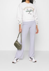 Ljusgrå sweatshirt med grafiken "WELLBEING"; ribbade ljuslila utsvängda byxor; grön axelväska; vita och svarta sportskor.