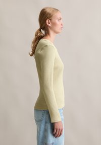 Haut côtelé à manches longues, vert clair, avec un col rond, silhouette ajustée et tissu texturé, associé à un jean en denim bleu clair.