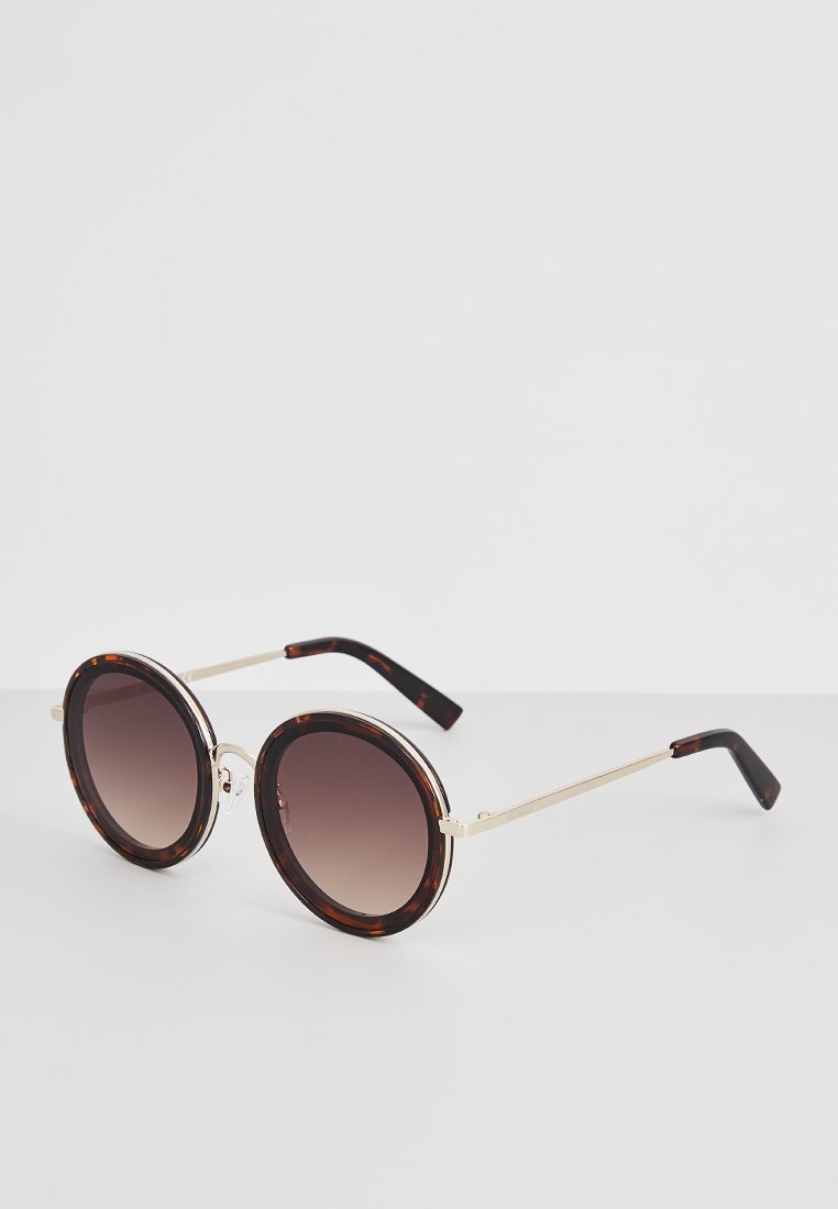 Occhiali da sole rotondi con montatura in tartaruga, lenti sfumate e sottili dettagli in metallo dorato ai lati. Superficie liscia e lucida.